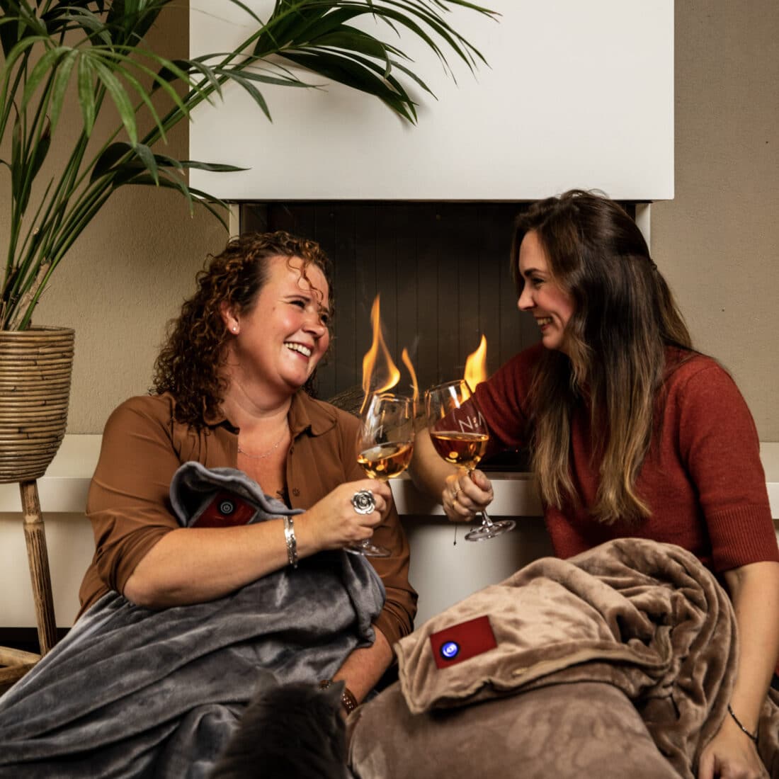 met vriendin voor de openhaard ontspannen met een glas wijn onder een zachte infrarood deken